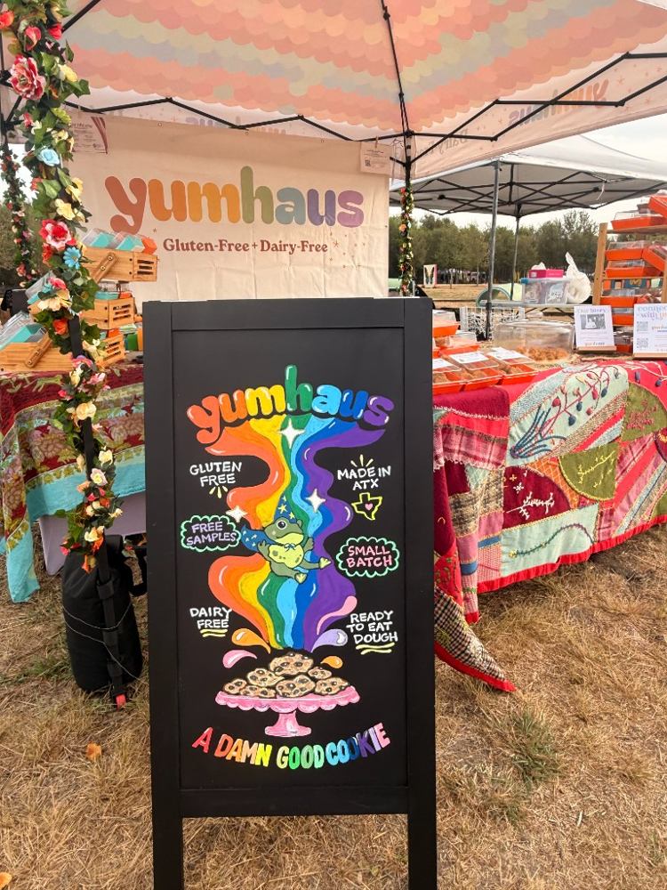 The Yumhaus farmers market booth in Austin with a hand-painted rainbow chalkboard sign that reads A damn good cookie